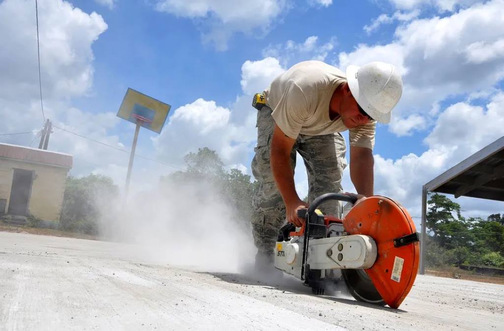 Outdoor construction scene showing a full-size circular saw in action on a deck frame, with safety gear and stable footing emphasized.
