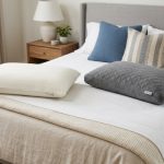 Side-by-side comparison of a white latex pillow and a gray memory foam pillow on a neatly made bed