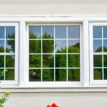 White triple-pane window with trees reflected in the glass set in a white wall.